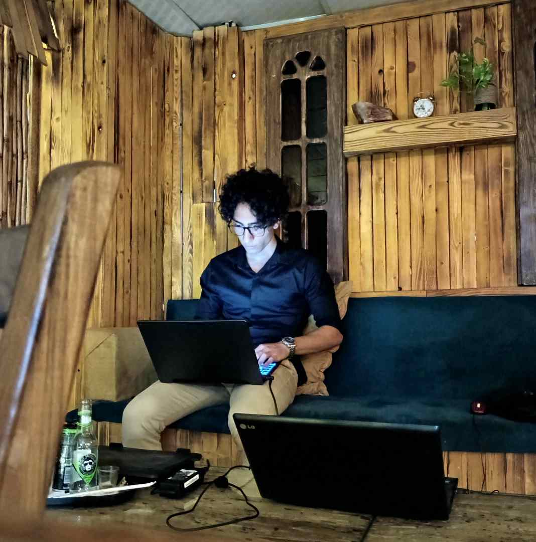 Mahyar is sit on a sofa and his laptop is on his laps, he's in a cafe